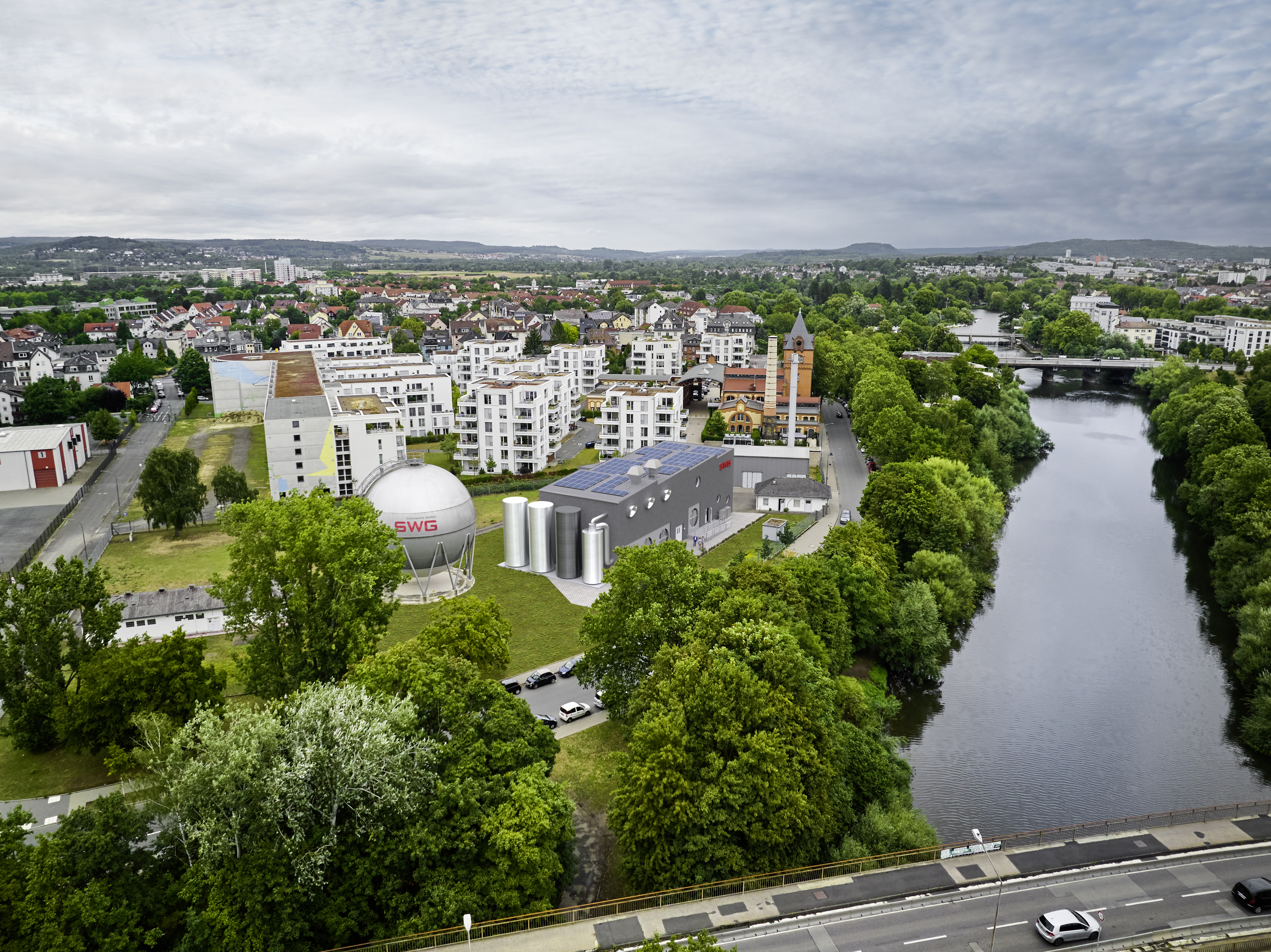 Aerial montage of the planned PowerLahn facility on the bank of the River Lahn, surrounded by trees and urban development in Gießen.